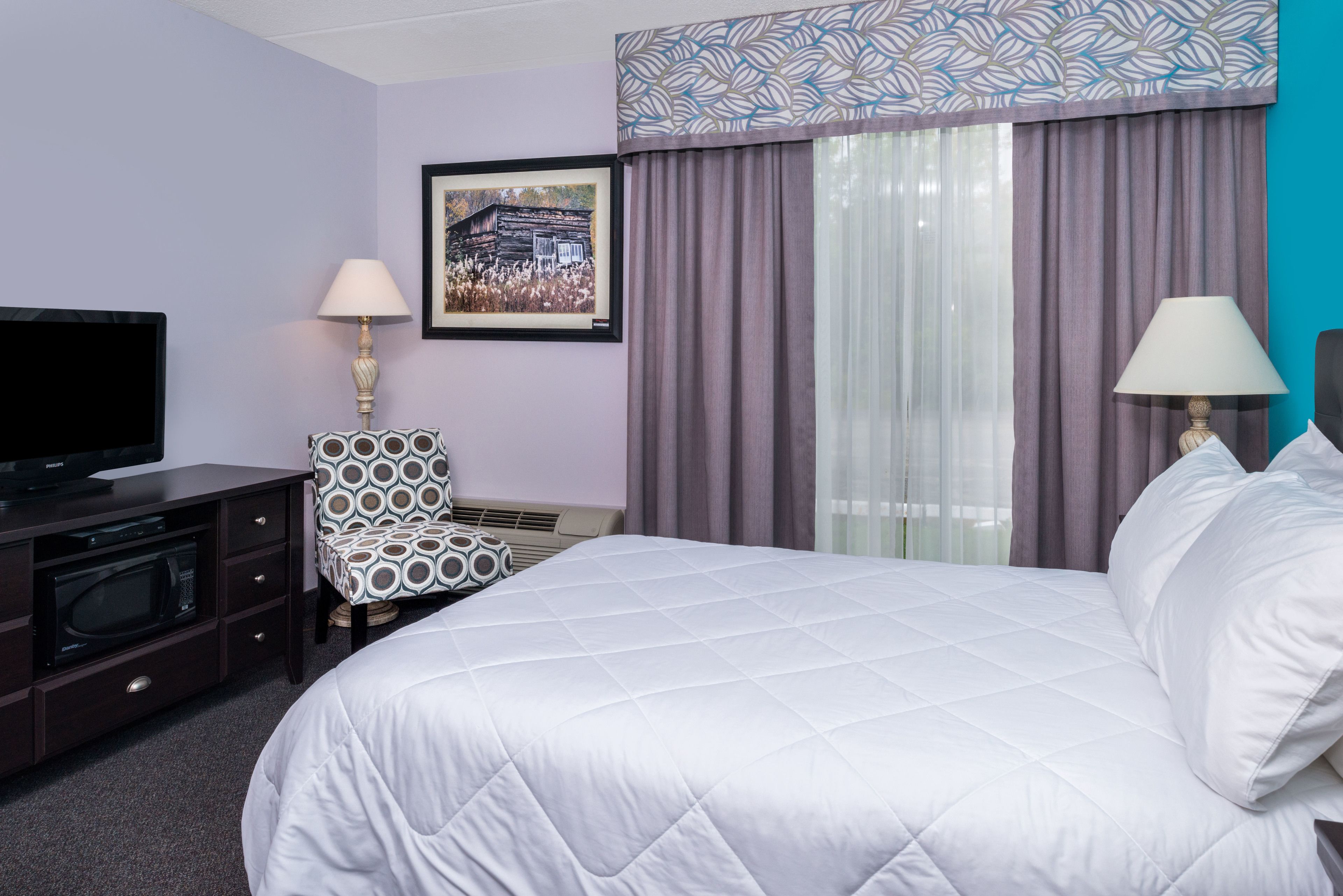 Une chambre d’hôtel avec un lit, une télévision, une chaise et un tableau au mur.