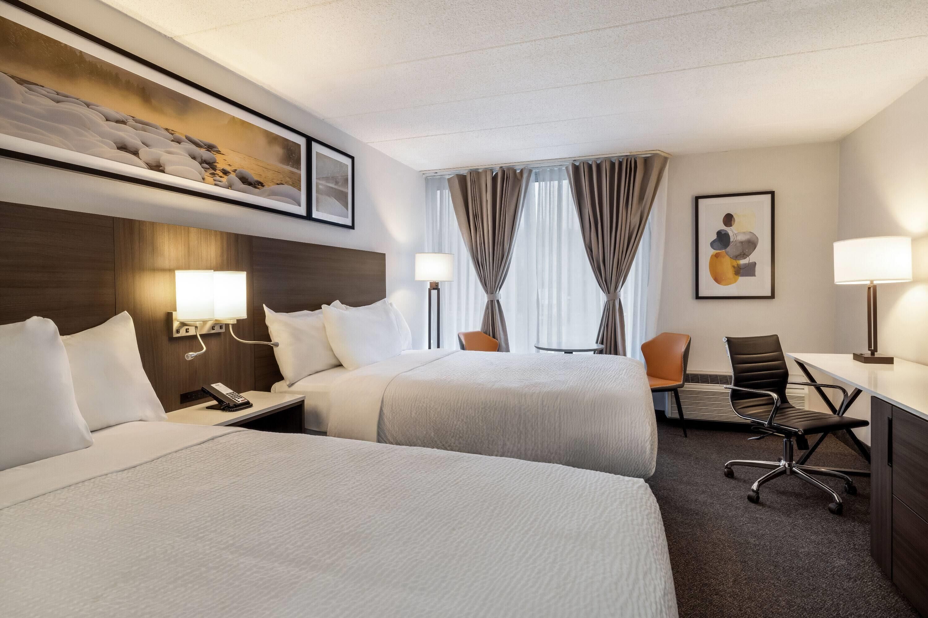 Una habitación de hotel con dos camas, un escritorio, una silla y un ventanal con cortinas.