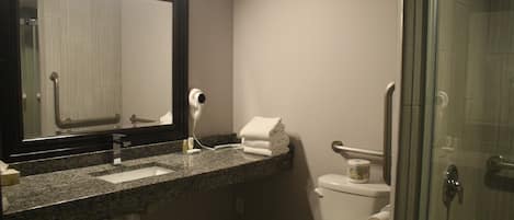 A bathroom with a granite countertop, a white toilet, a glass shower enclosure, and a mirror with a black frame.