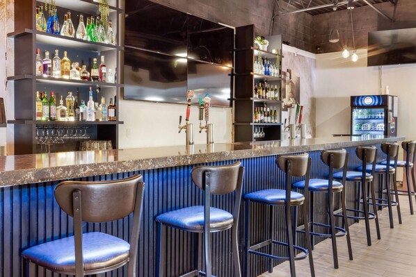 Zona de bar con múltiples estantes de botellas de licor, una barra y varios taburetes.