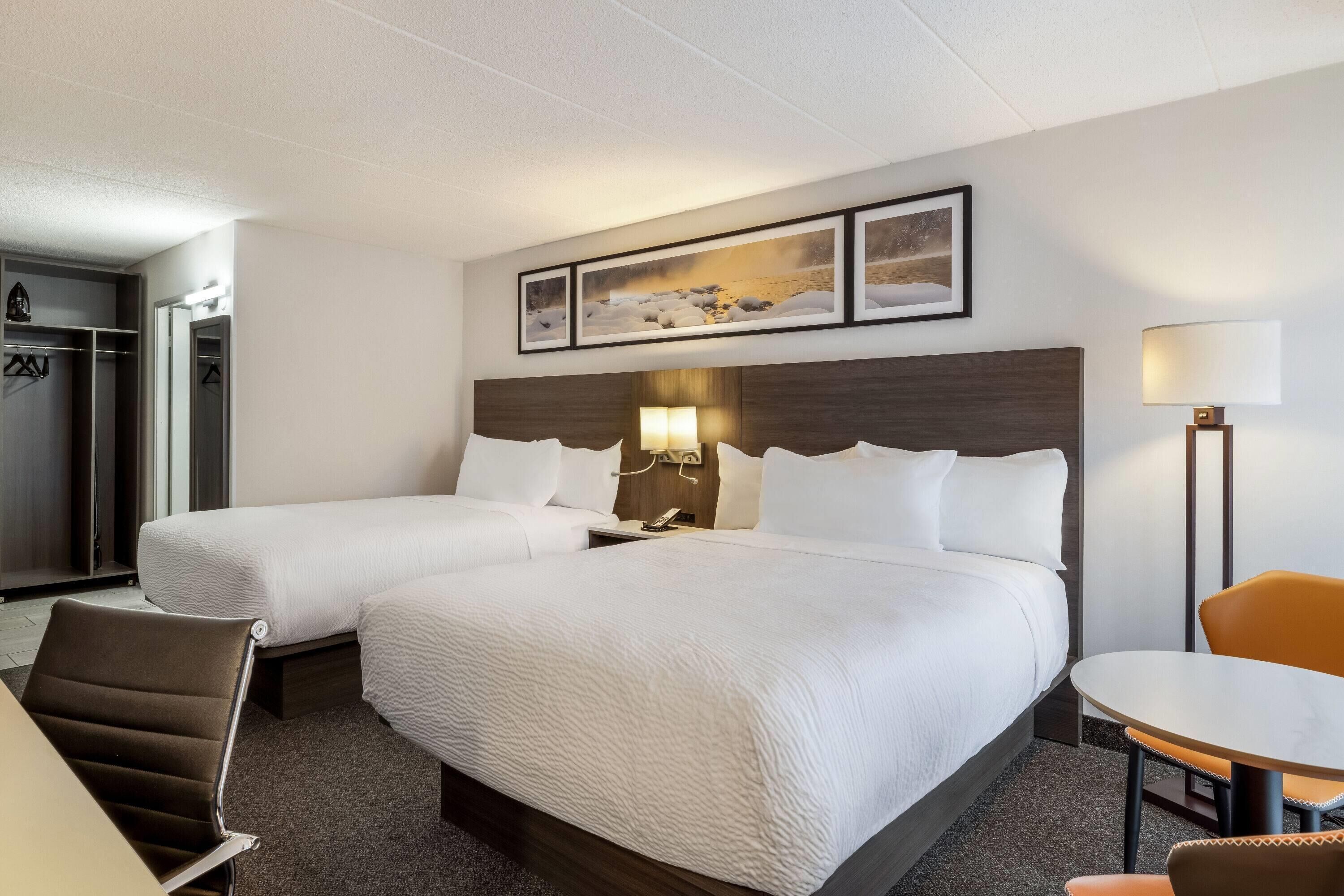 Ein Hotelzimmer mit zwei Betten, einem Schreibtisch, einem Stuhl, einer Lampe und einem Kleiderhaken.
