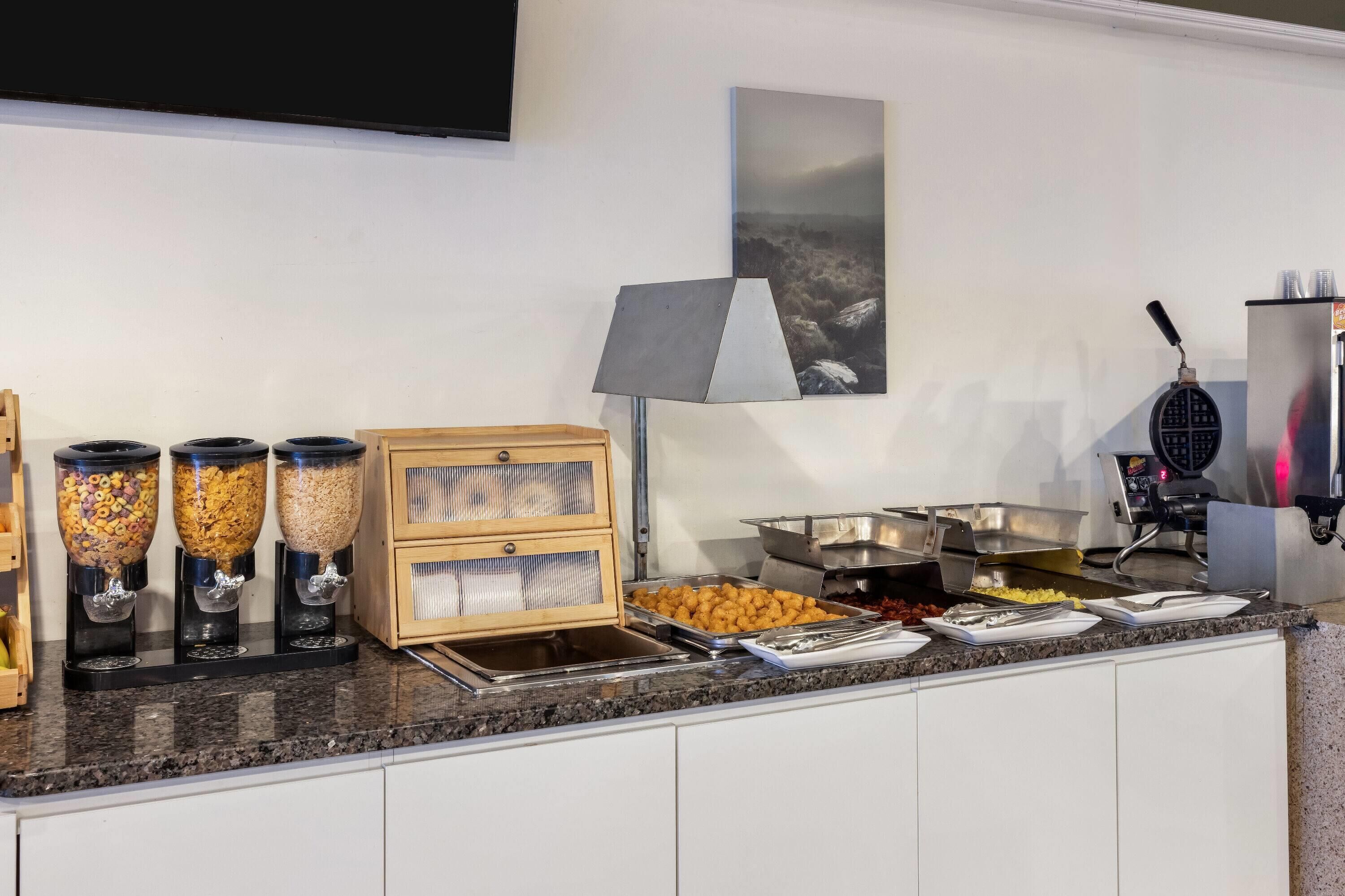 Montaje de bufé con diferentes dispensadores de alimentos, una máquina para gofres y un televisor de pantalla plana en la pared.