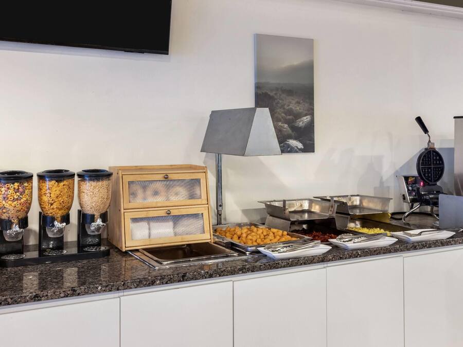 Montaje de bufé con diferentes dispensadores de alimentos, una máquina para gofres y un televisor de pantalla plana en la pared.