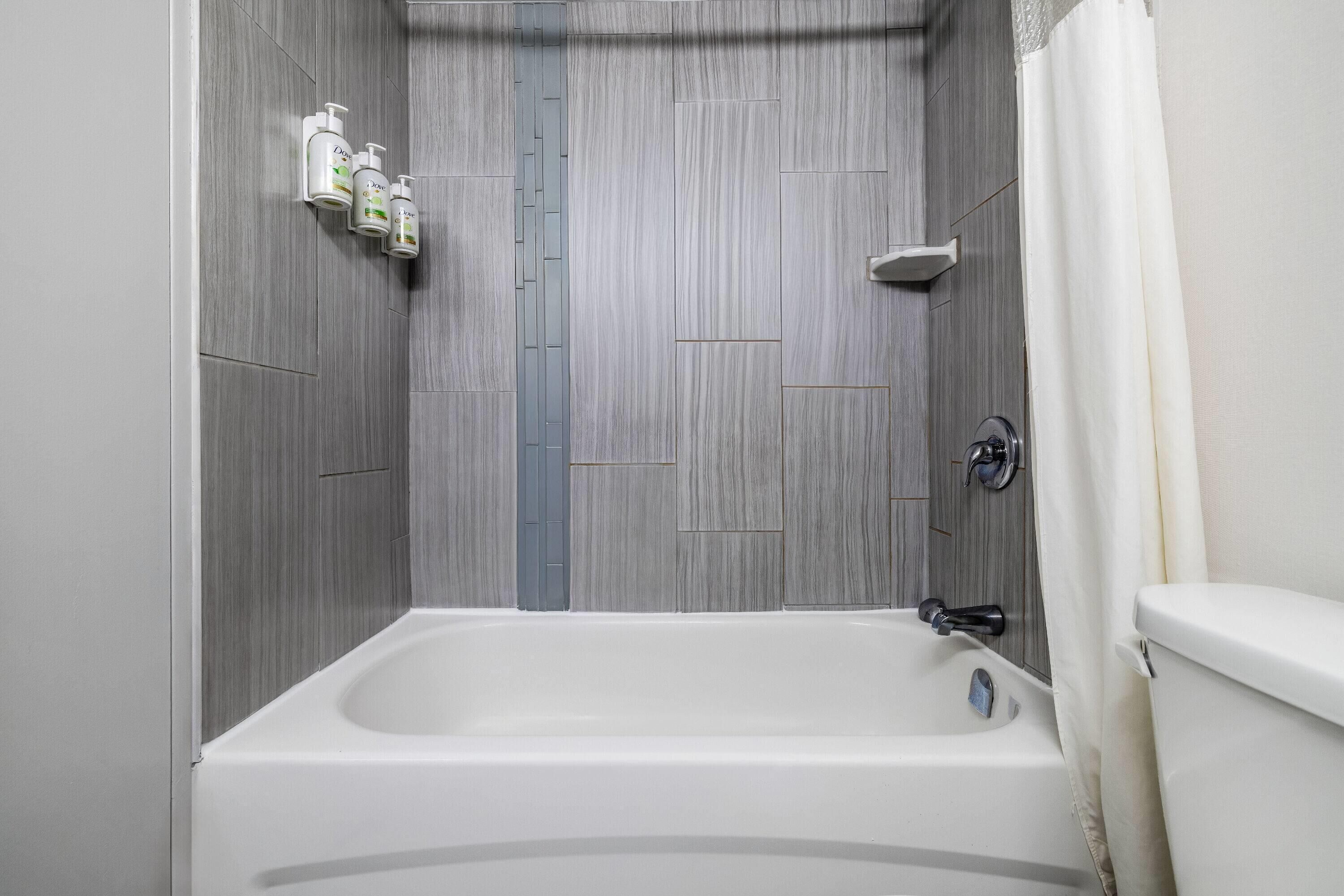 Une salle de bain avec une baignoire, des toilettes et trois bouteilles de shampoing accrochées au mur.