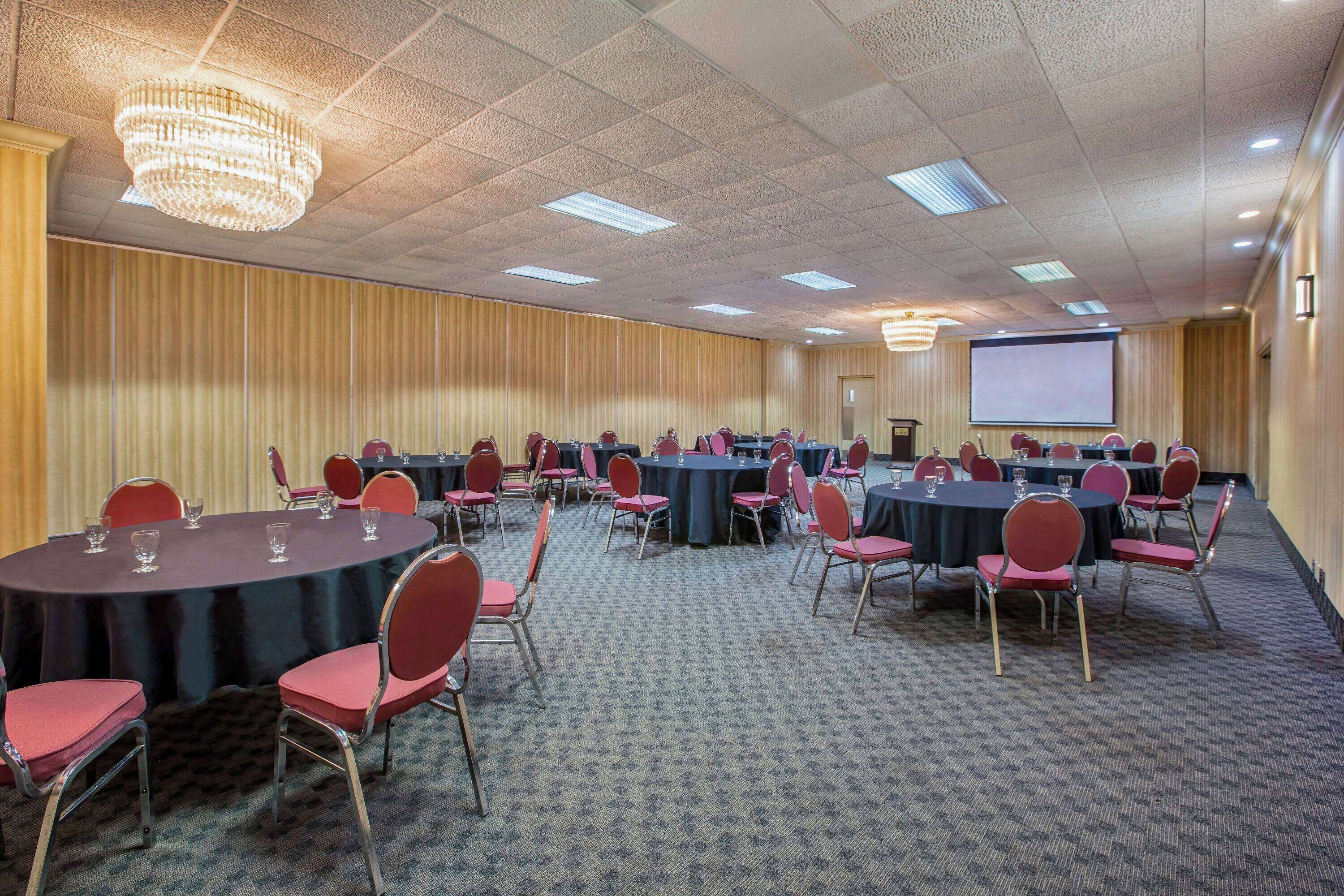A conference room with multiple round tables, red chairs, and a large screen.