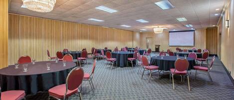 A conference room with multiple round tables, red chairs, and a large screen.