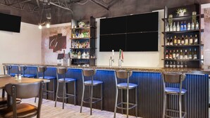 Zona de bar con taburetes, barra, estantes con botellas y un televisor en la pared.