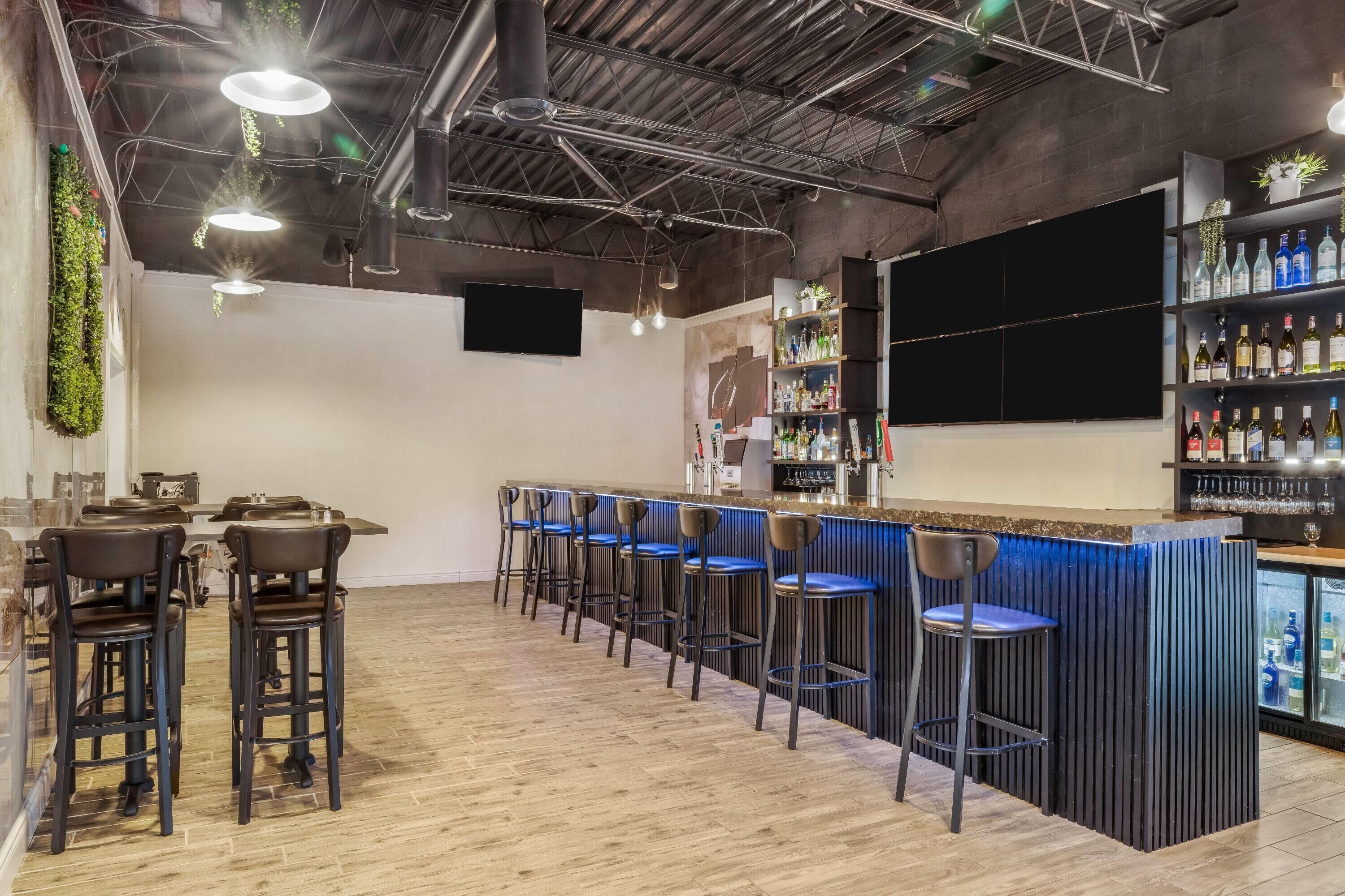 Una zona de bar con taburetes, una barra y estantes llenos de botellas.
