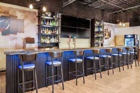 A bar area with a counter, multiple stools, shelves with bottles, and a refrigerator.. Days Inn by Wyndham Sudbury & Conference Centre