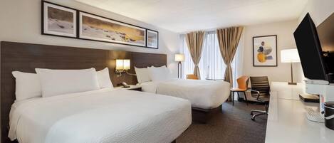 A hotel room with two beds, a desk, a chair, a TV, and artwork on the walls.