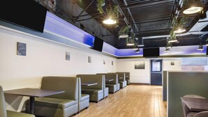 A restaurant with booth seating, a flat-screen TV, hanging plants, and pendant lighting.