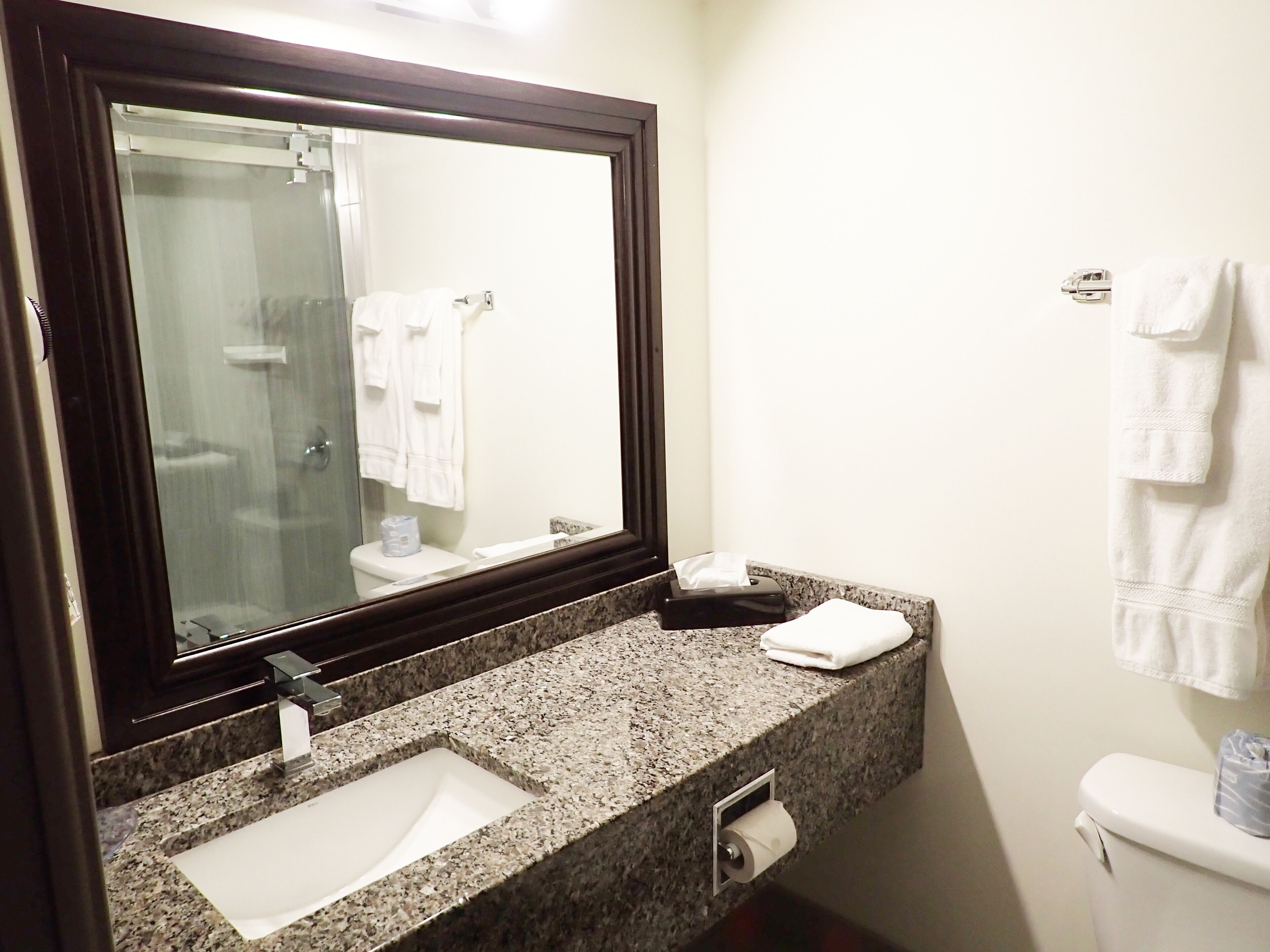 A bathroom with a granite countertop, a sink, a mirror, a toilet, and a towel rack.