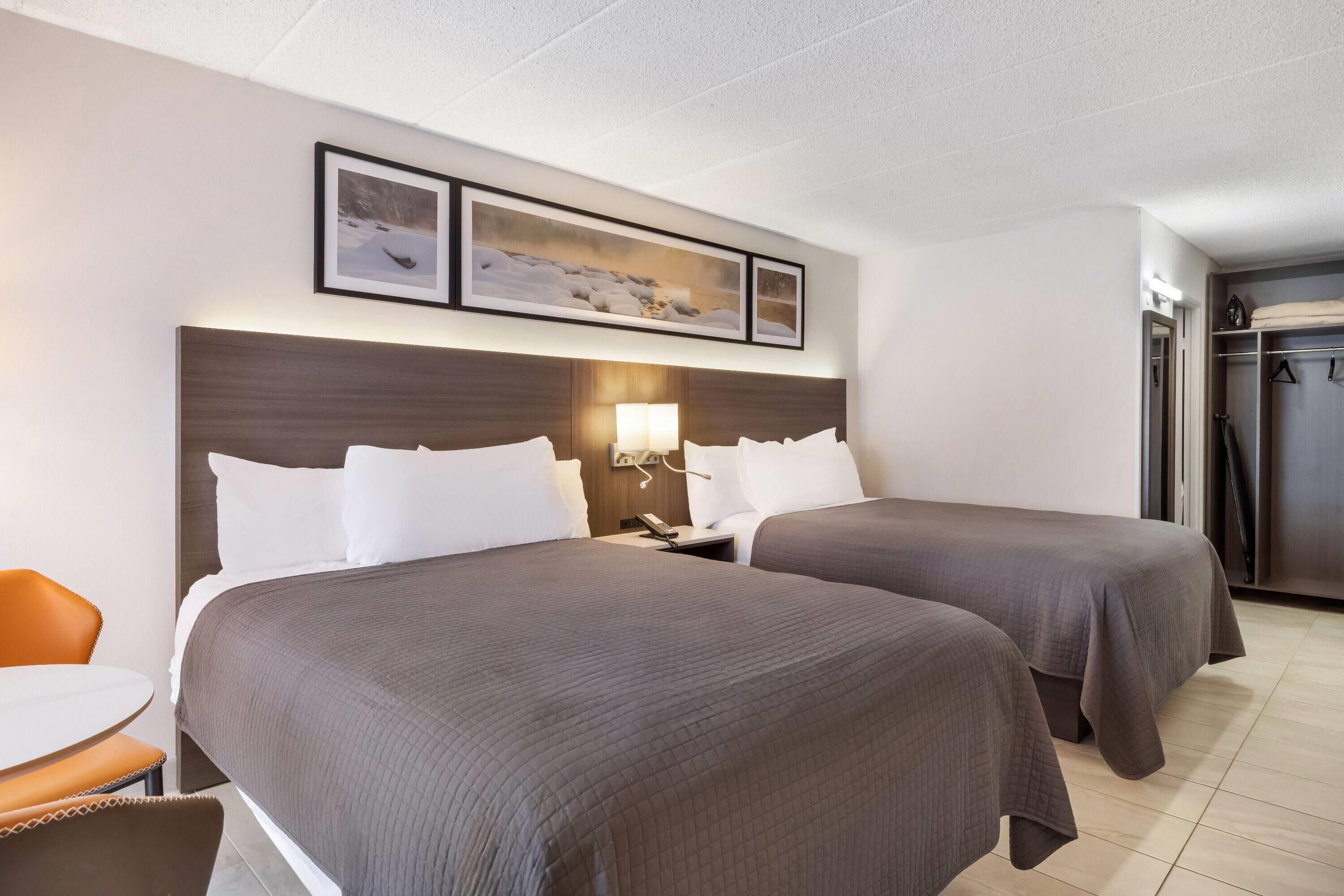 A hotel room with two beds, a desk, and a chair. There is a coat closet and a refrigerator.