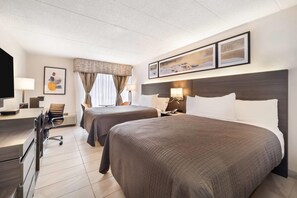 Une chambre d’hôtel avec deux lits, un bureau, une chaise, une télévision et des tableaux encadrés au mur.