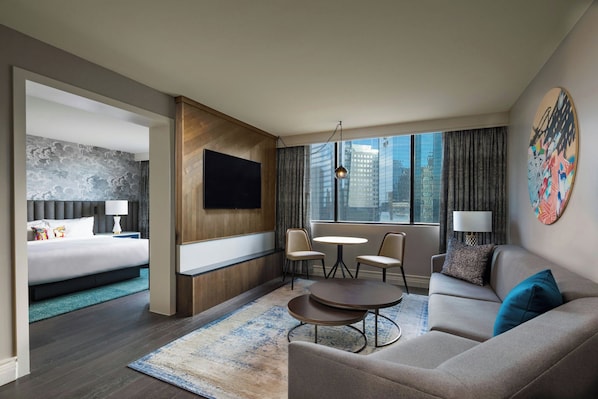 A modern hotel room with a bed, a sofa, a small table, and a TV.