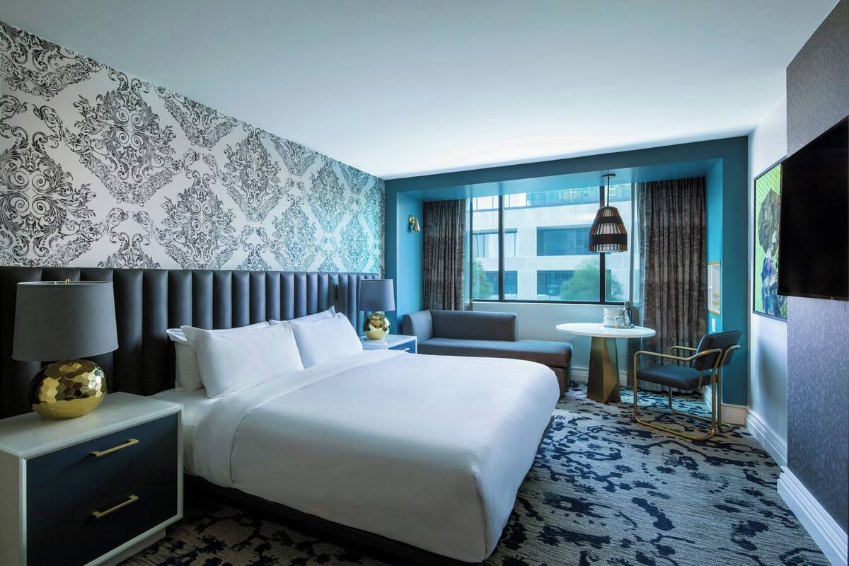 A modern hotel room with a large bed, a seating area, and a view of the city.