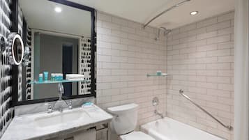 A modern bathroom with a white sink, a toilet, and a bathtub. There is a glass shelf above the sink and a mirror with a black frame.