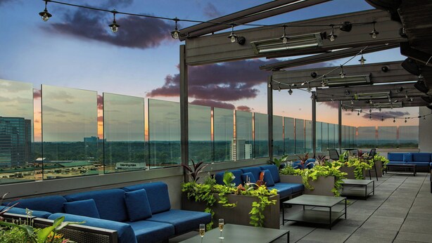 Un lounge sul tetto con sedute blu, una ringhiera in vetro e vista sulla città.