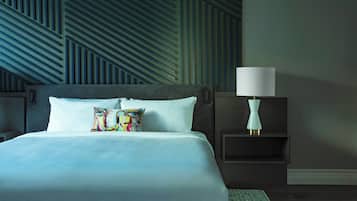 Una habitación de hotel moderna con una cama grande, un cojín colorido, una mesita de noche con una lámpara y un papel tapiz de diseño geométrico.