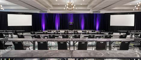 A conference room with a stage, large screens, and rows of tables and chairs.
