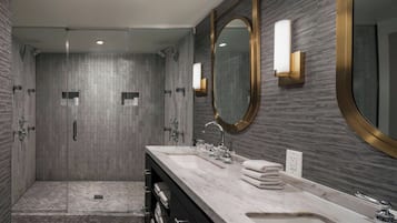 A modern bathroom with a walk-in shower, dual sinks, and a large mirror with a gold frame.