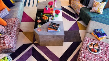 Una sala de estar moderna con un tapete de diseño geométrico, una mesa de centro con libros y objetos decorativos, y un sofá con cojines estampados.