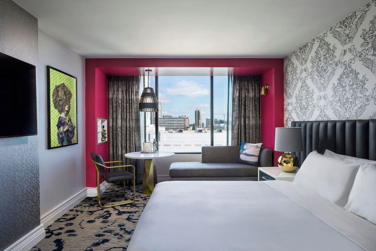 A hotel room with a large bed, a seating area with a view, a small table, and a TV.