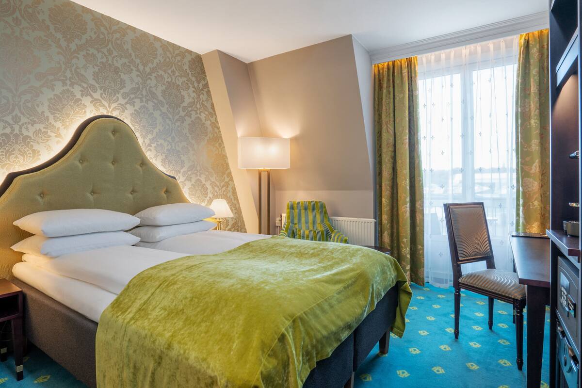 A hotel room with a large bed, a nightstand, a chair, a desk, and a window with curtains.
