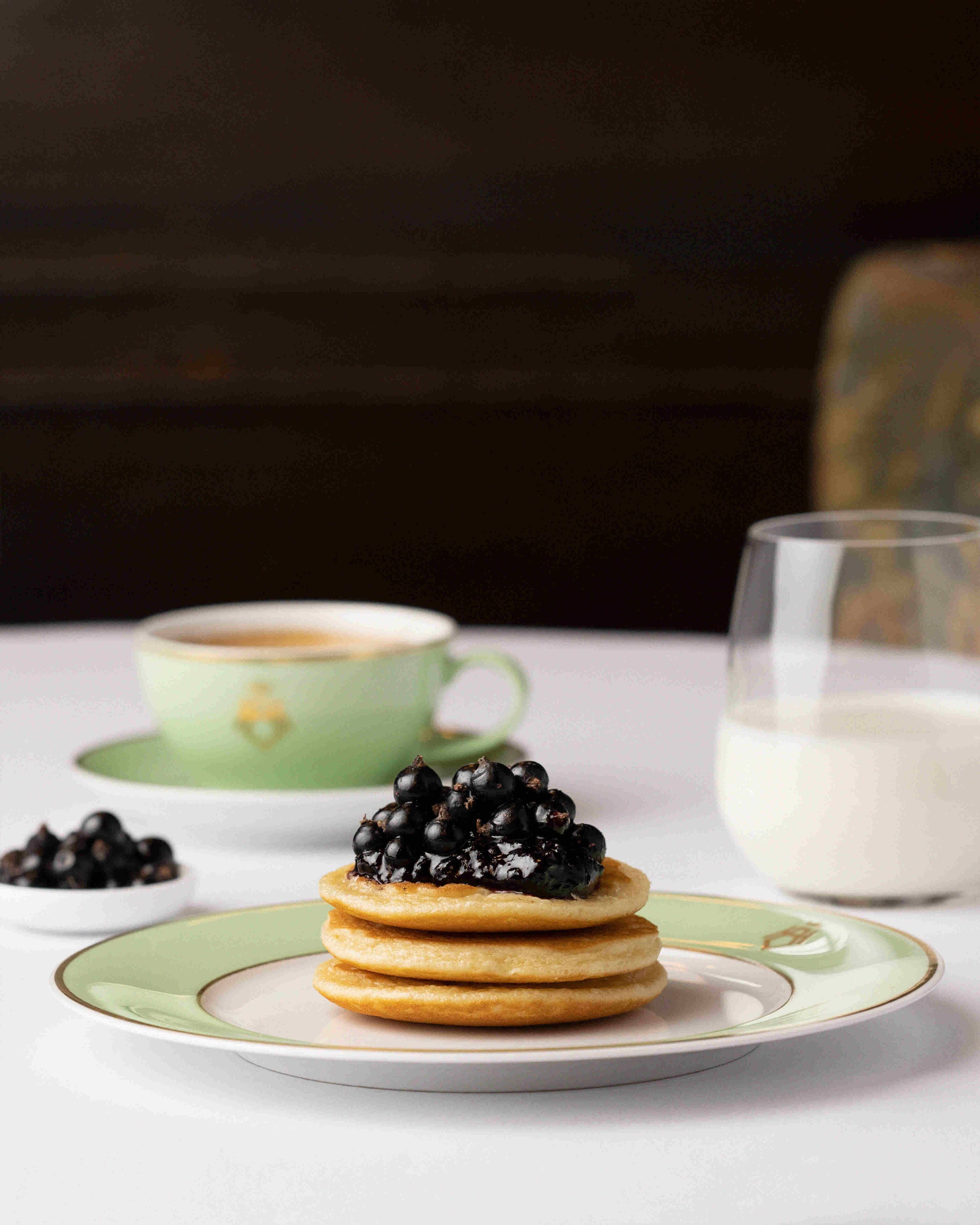 A stack of pancakes with blackberries on a plate, a cup of coffee, and a glass of milk.