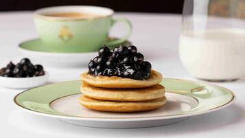 A stack of pancakes with blackberries on a plate, a cup of coffee, and a glass of milk.
