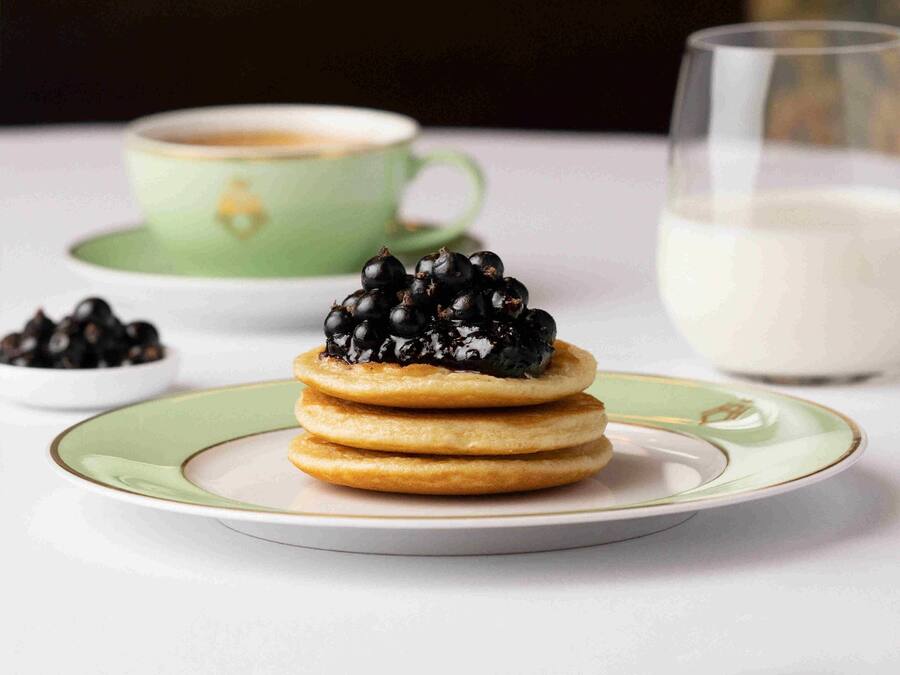 A stack of pancakes with blackberries on a plate, a cup of coffee, and a glass of milk.