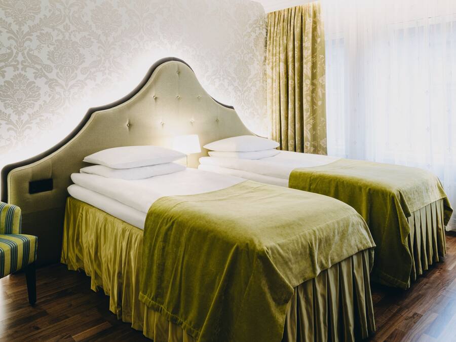 Habitación de hotel con dos camas, suelo de madera y papel tapiz estampado.