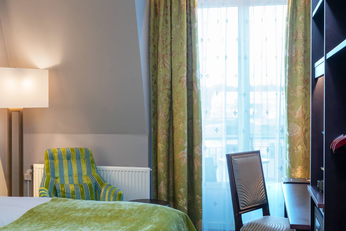 A hotel room with a bed, a chair, a table, a lamp, and a window with curtains.