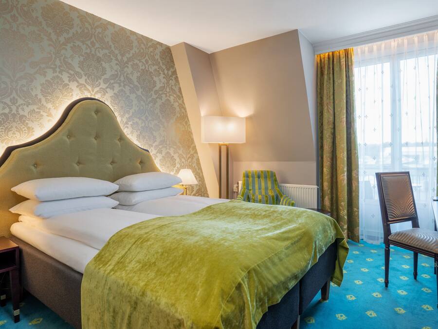 Habitación de hotel con una cama grande, una silla, un escritorio y un ventanal con cortinas.
