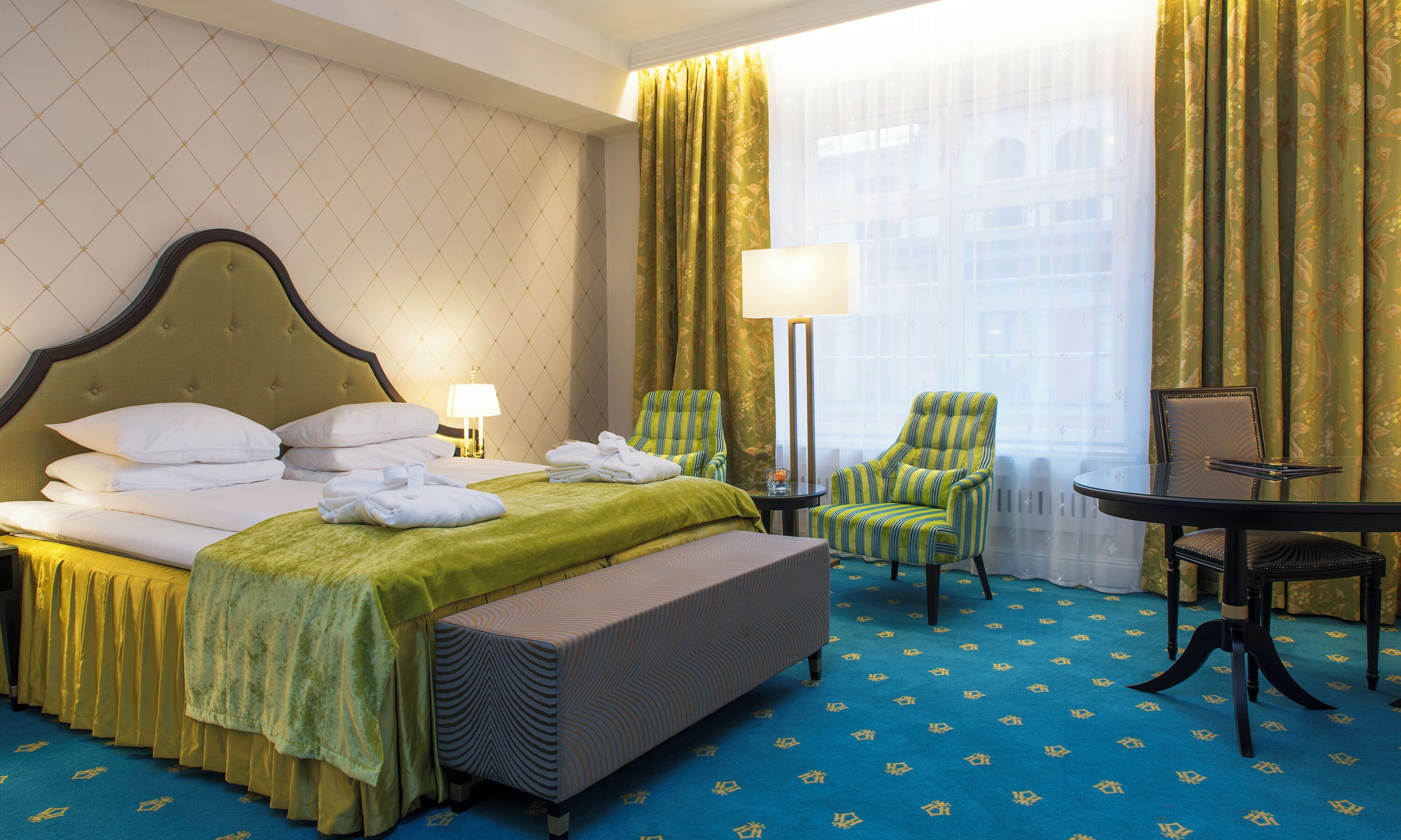 A hotel room with a bed, two chairs, a table, and a window with curtains.
