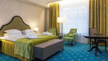 A hotel room with a bed, two chairs, a table, and a window with curtains.