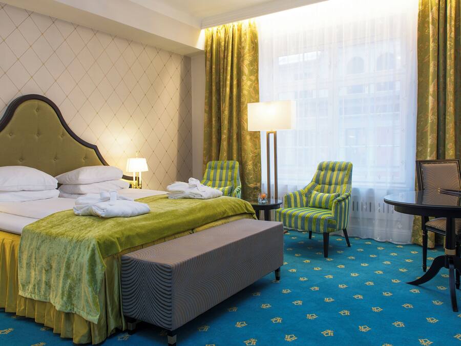 A hotel room with a bed, two chairs, a table, and a window with curtains.
