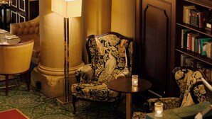 A luxurious lobby with ornate columns, a chandelier, a patterned armchair, and a bookshelf. - Hotel Bristol (Oslo)