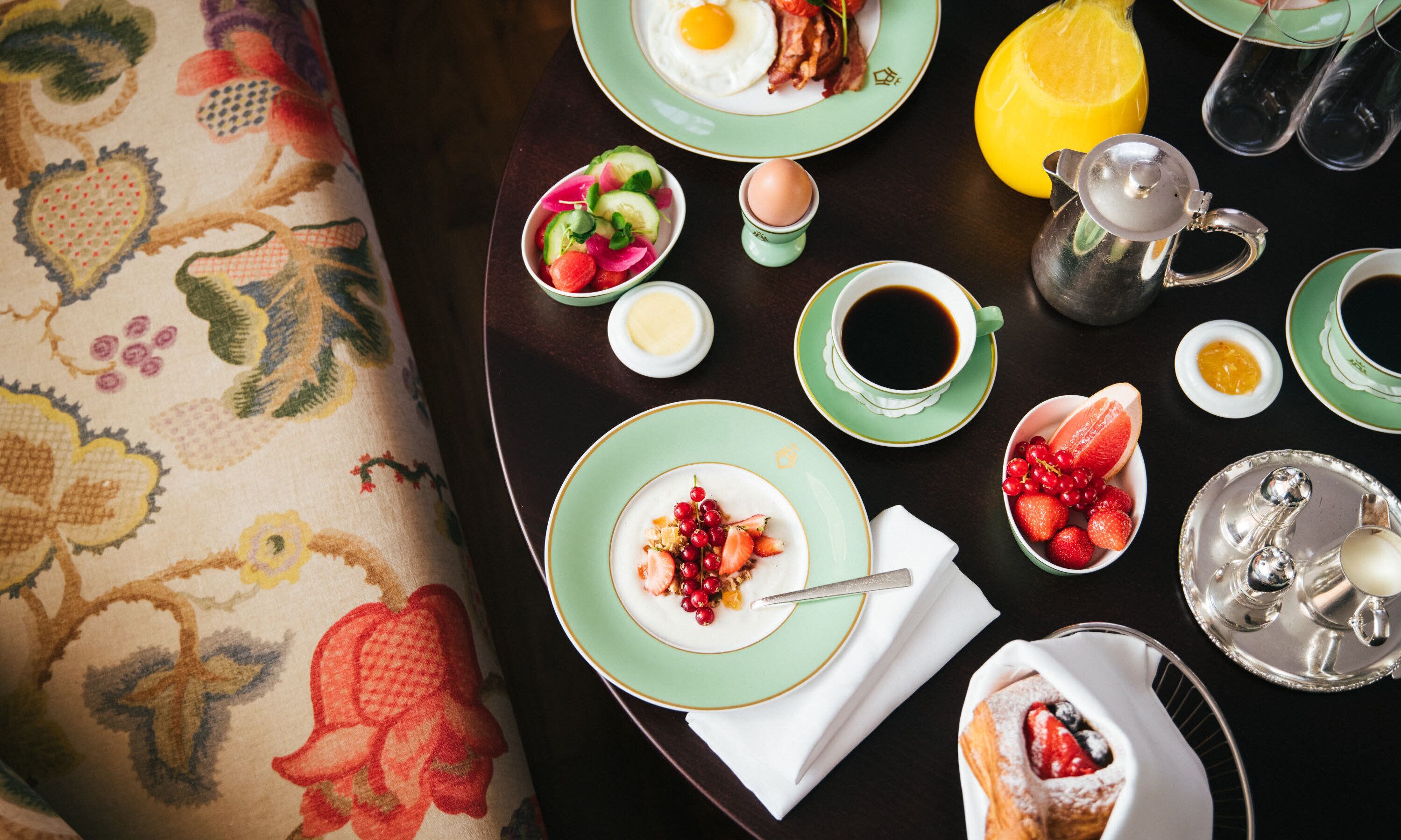 Uma mesa de café da manhã com pratos de comida, um jarro de suco de laranja e um coador de café.