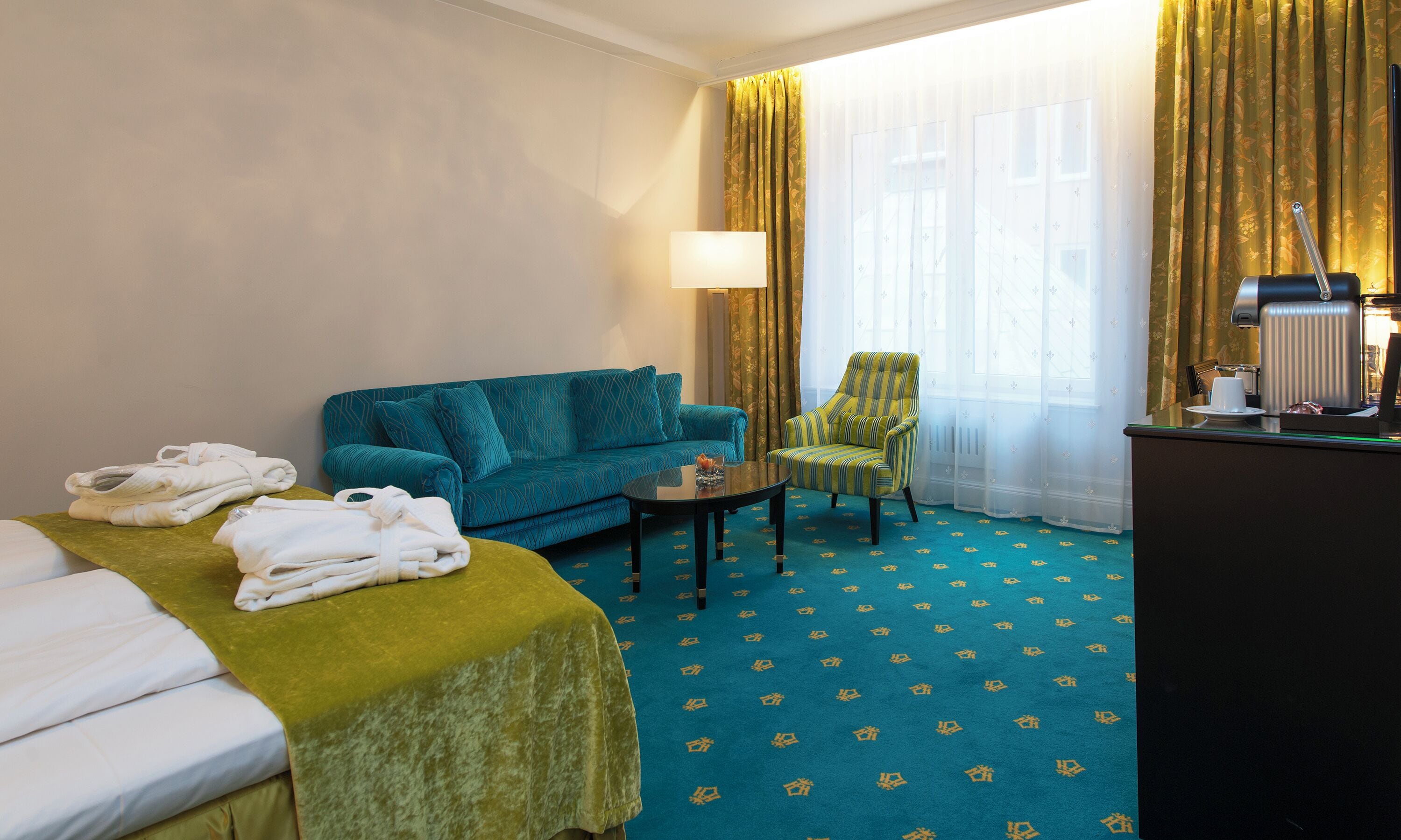 Una habitación de hotel con cama, sofá, sillón, mesa de centro y escritorio con lámpara.