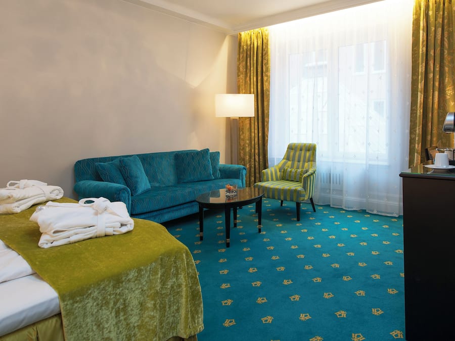 Una habitación de hotel con cama, sofá, sillón, mesa de centro y escritorio con lámpara.