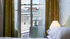 A hotel room with a bed, a balcony with a view of the city, and a window with curtains. - Hotel Bristol (Oslo)