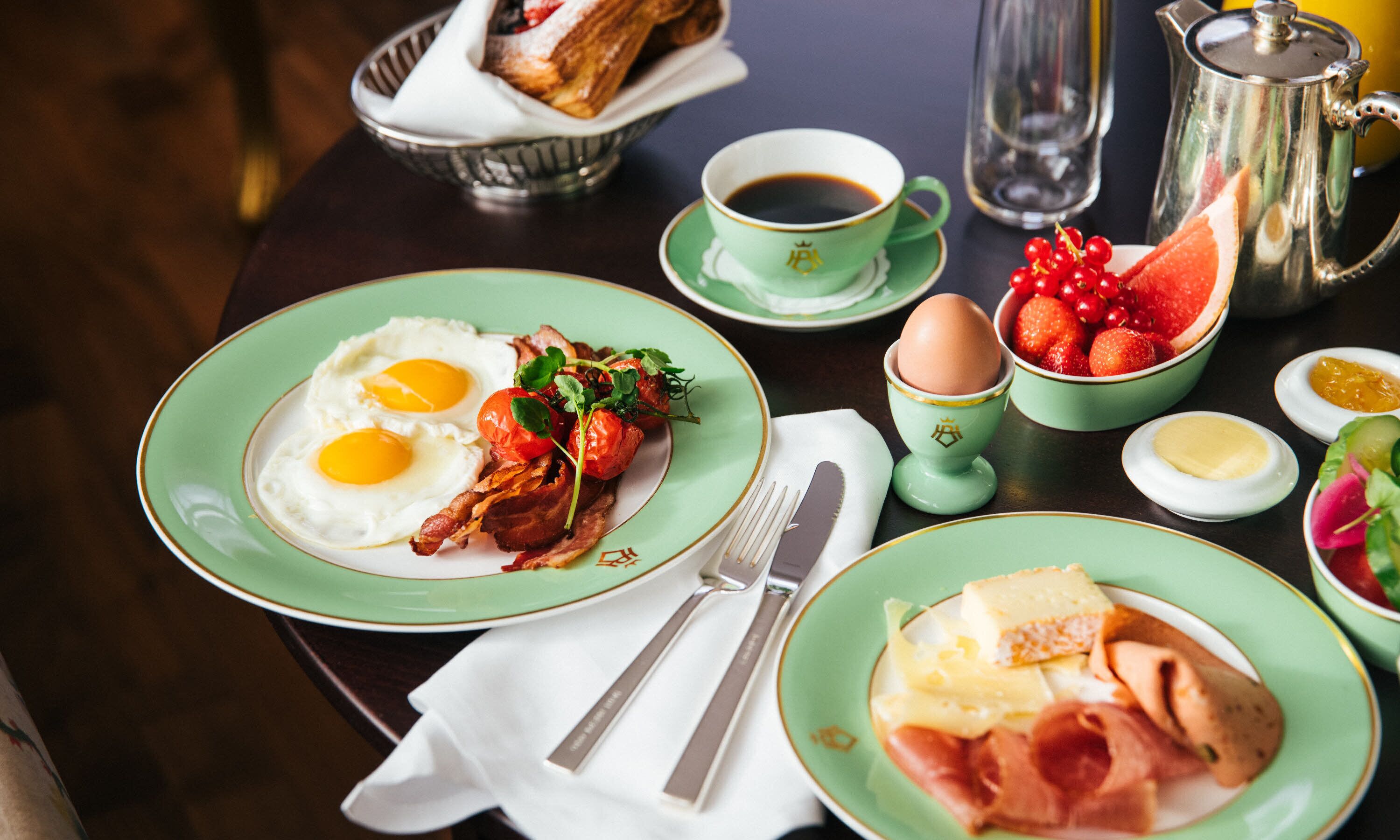Een ontbijtsetting met borden eieren, spek en toast, een kop koffie en verschillende toevoegingen.