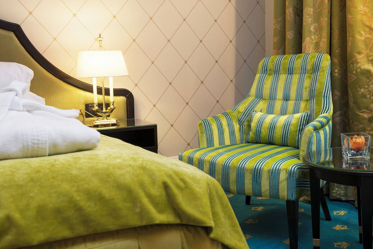 A hotel room with a bed, a chair, a table, and a lamp.