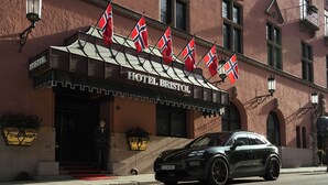 A hotel entrance with flags, a red carpet, and a black car parked in front. - Hotel Bristol (Oslo)