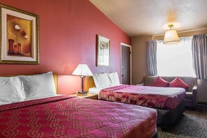 Quarto de hotel com duas camas, uma mesa de cabeceira com abajur, um quadro na parede e uma janela com cortinas.