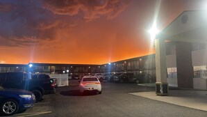 A parking lot with several cars and a building with a flat roof and large windows.