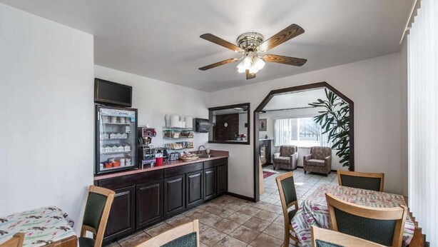 A compact kitchen with dark cabinets, a refrigerator, and a microwave. There is a dining area with a table and chairs, and a ceiling fan above.