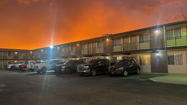 A motel with multiple parking spaces and a row of vehicles parked in front.