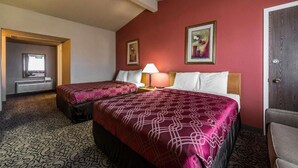 A hotel room with two beds, a nightstand, a lamp, and a door.